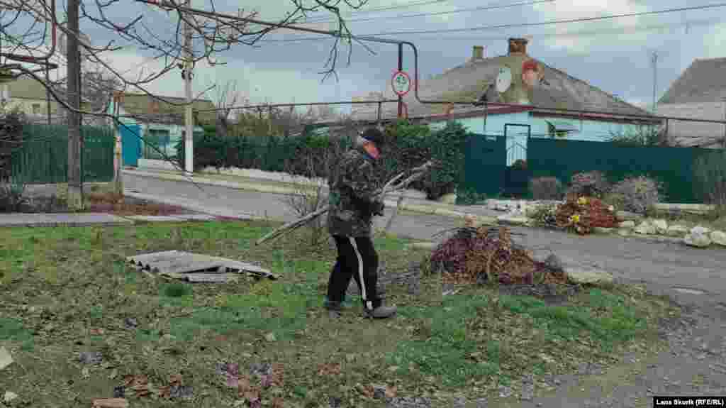 Мужчина собирает на улице перед домом упавшие после ветра ветки