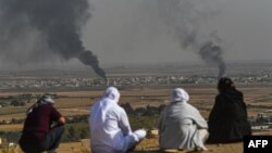 Люди смотрят, как поднимается дым в сирийском городе Рас-эль-Айн. Фотография сделана с турецкой стороны границы в Джейланпынаре 11 октября 2019 года, на третий день военной операции Турции против курдских сил. 